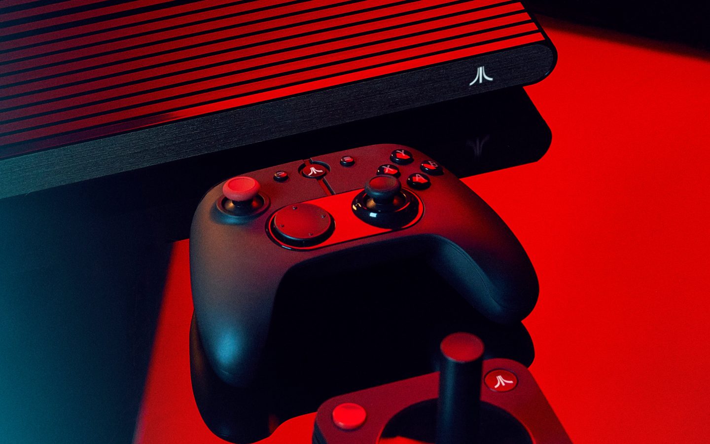 Atari VCS et ses manettes photographiées sur fond rouge, visuel officiel Atari